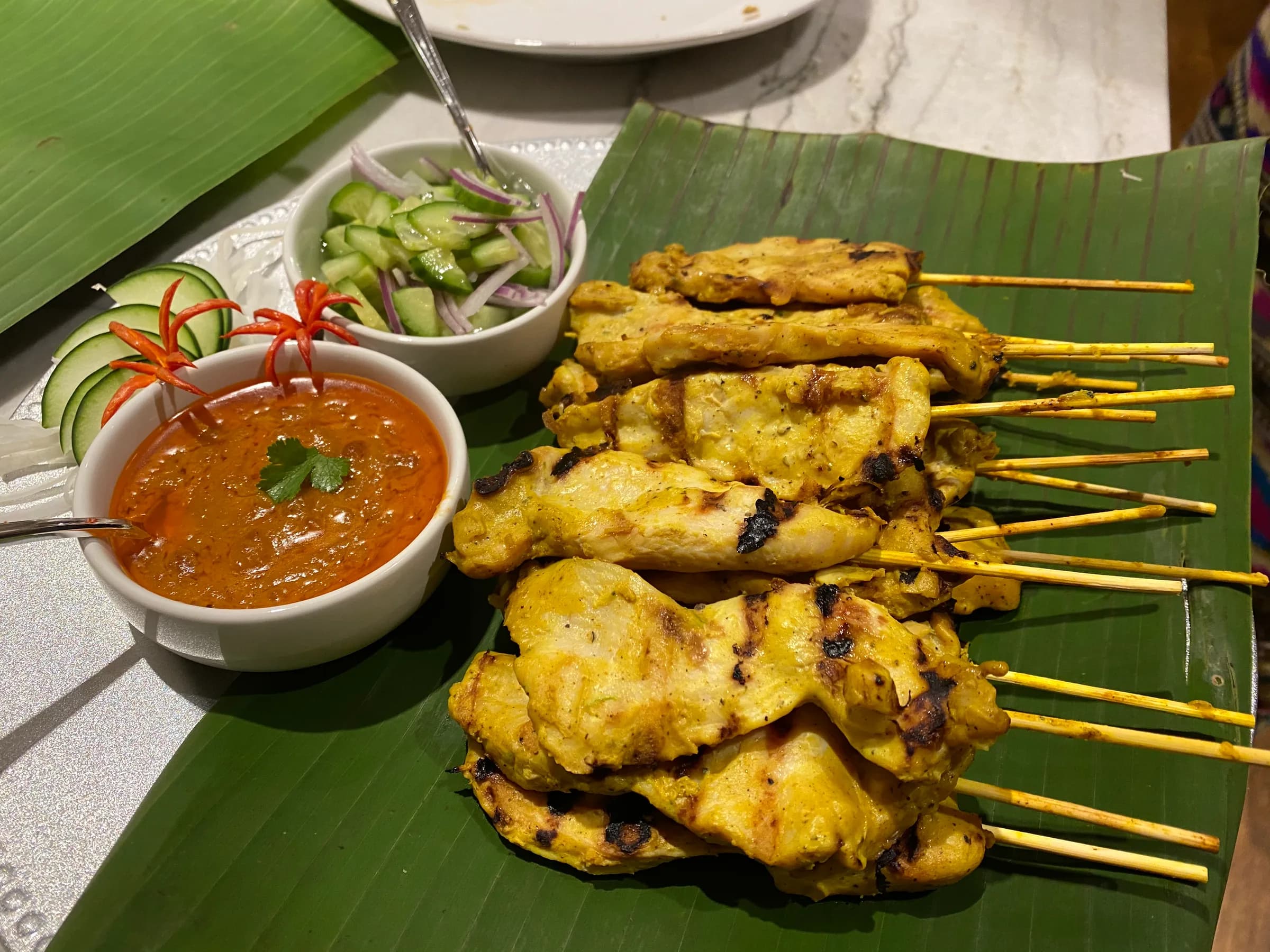 Chicken satay on a banana leaf with peanut sauce and cucumber relish