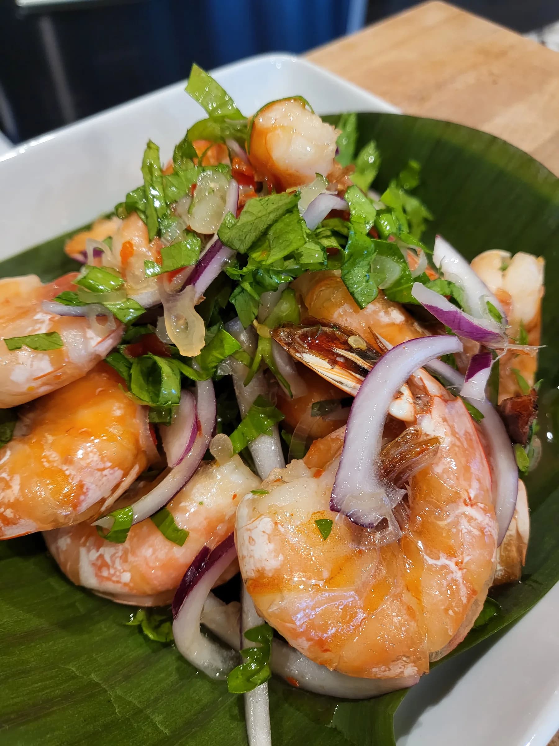 Whole prawns over herb salad with red onion, on a banana leaf