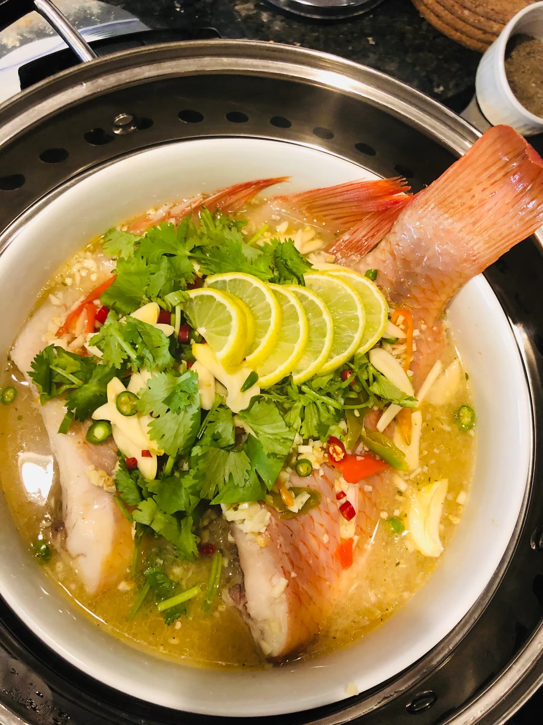 A whole steamed fish under lime slices, chili and coriander